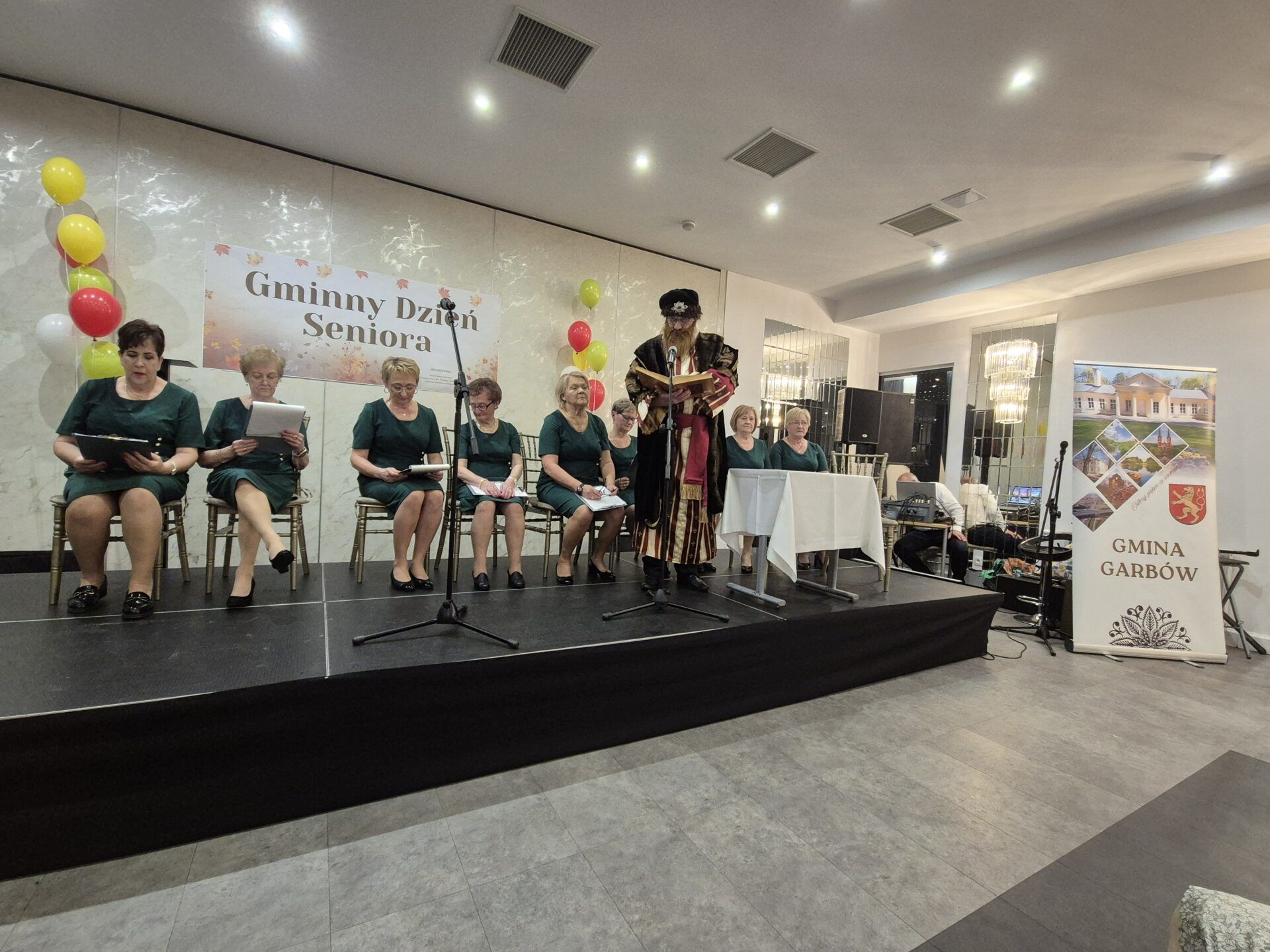 Seniorzy z Koła Rencistów i emerytów w zagrodach biorący udział w Narodowym Czytaniu podczas Gminnego Dnia Seniora