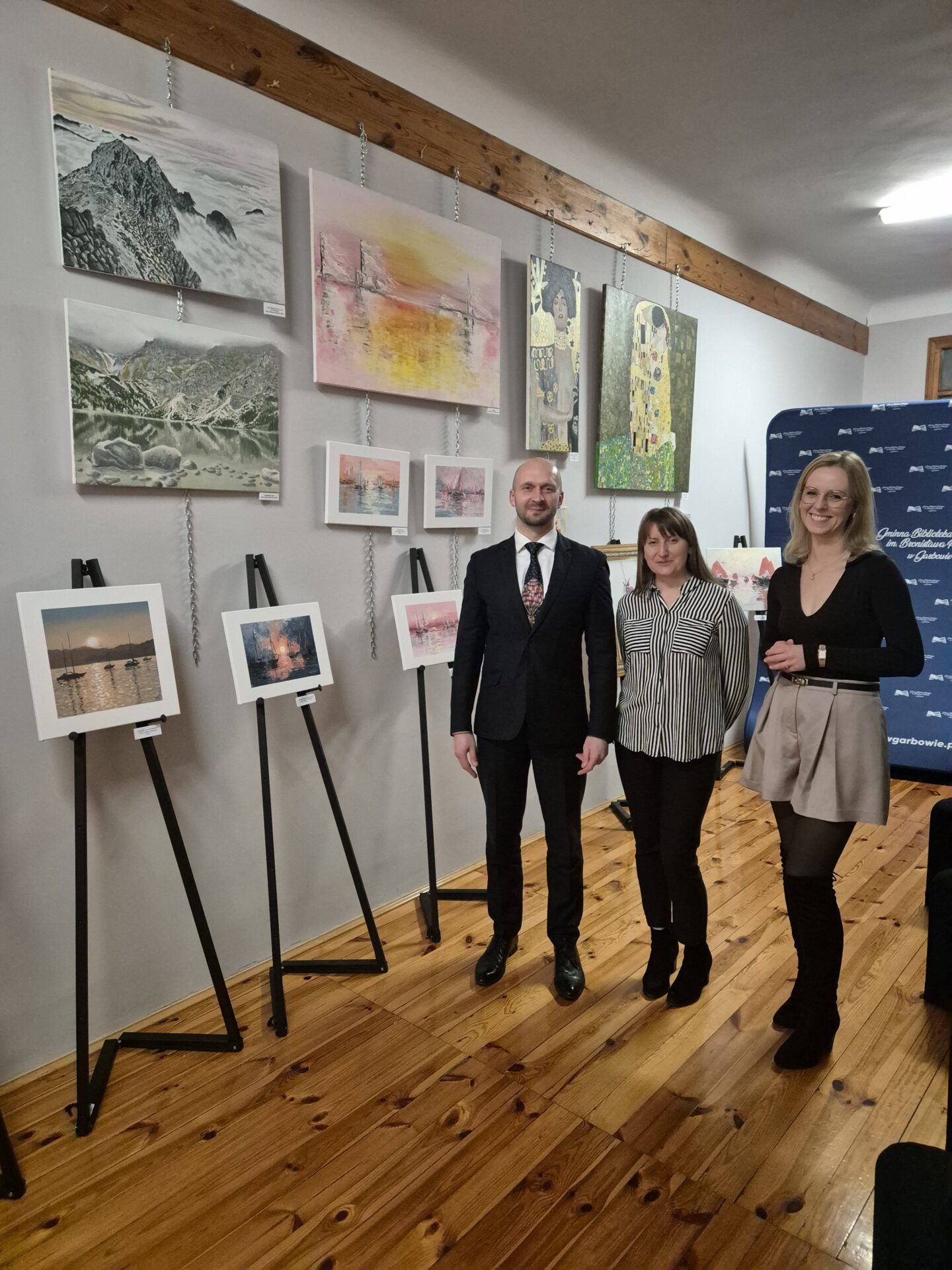 Dwie kobiety i mążczyzna na tle obrazów.