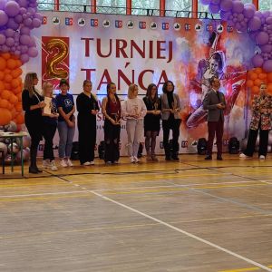 osiem osób na tle baneru Turniej Tańca ozdobionego balonami