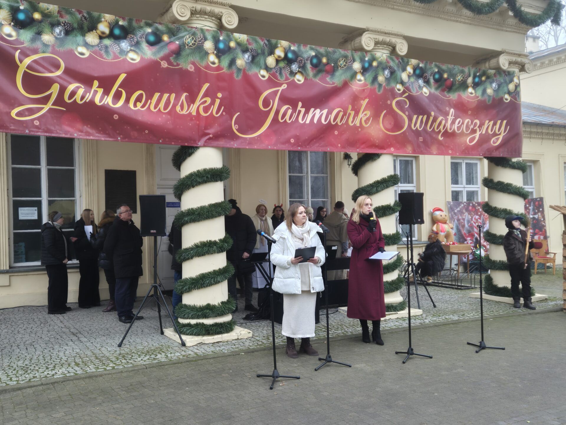 Panie prowadzące Garbowski jarmark Świąteczny na tle zabytkowego pałacu. Napis Garbowski Jarmark Świateczny.