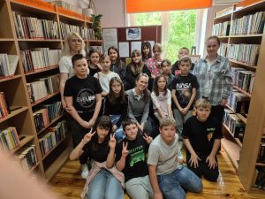 Grupa dzieci i trzy osoby dorosłe na tle regałów z książkami.