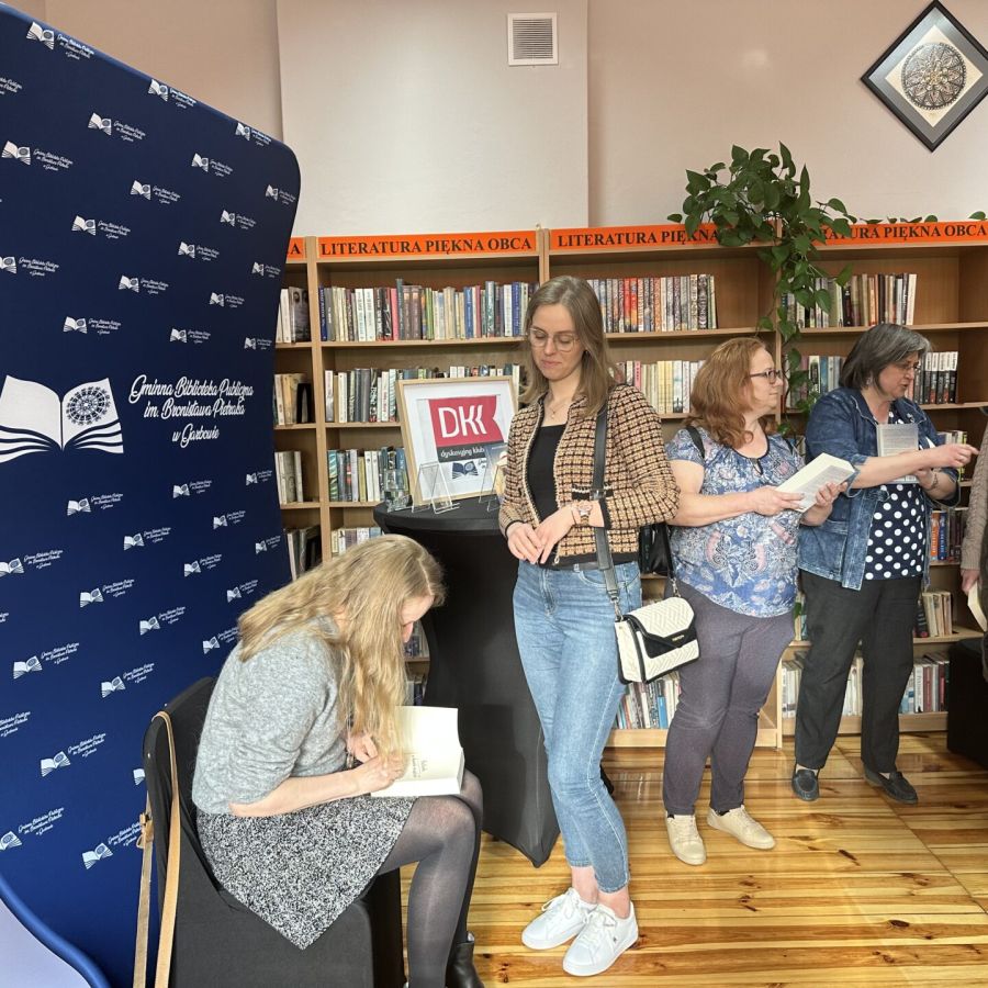 Cztery czytelniczki czekające na autograf agaty Kołakowskiej podczas spotkania autorskiego w bibliotece.