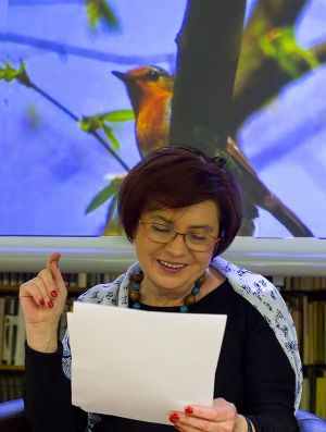 Czytająca poetka Ewa Pilipczuk na tle zdjęcia z ptakiem siedzącym na gałęzi.