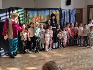 Grupa dzieci wraz z aktorami podczas przedstawienia teatralnego "Latający Kufer"