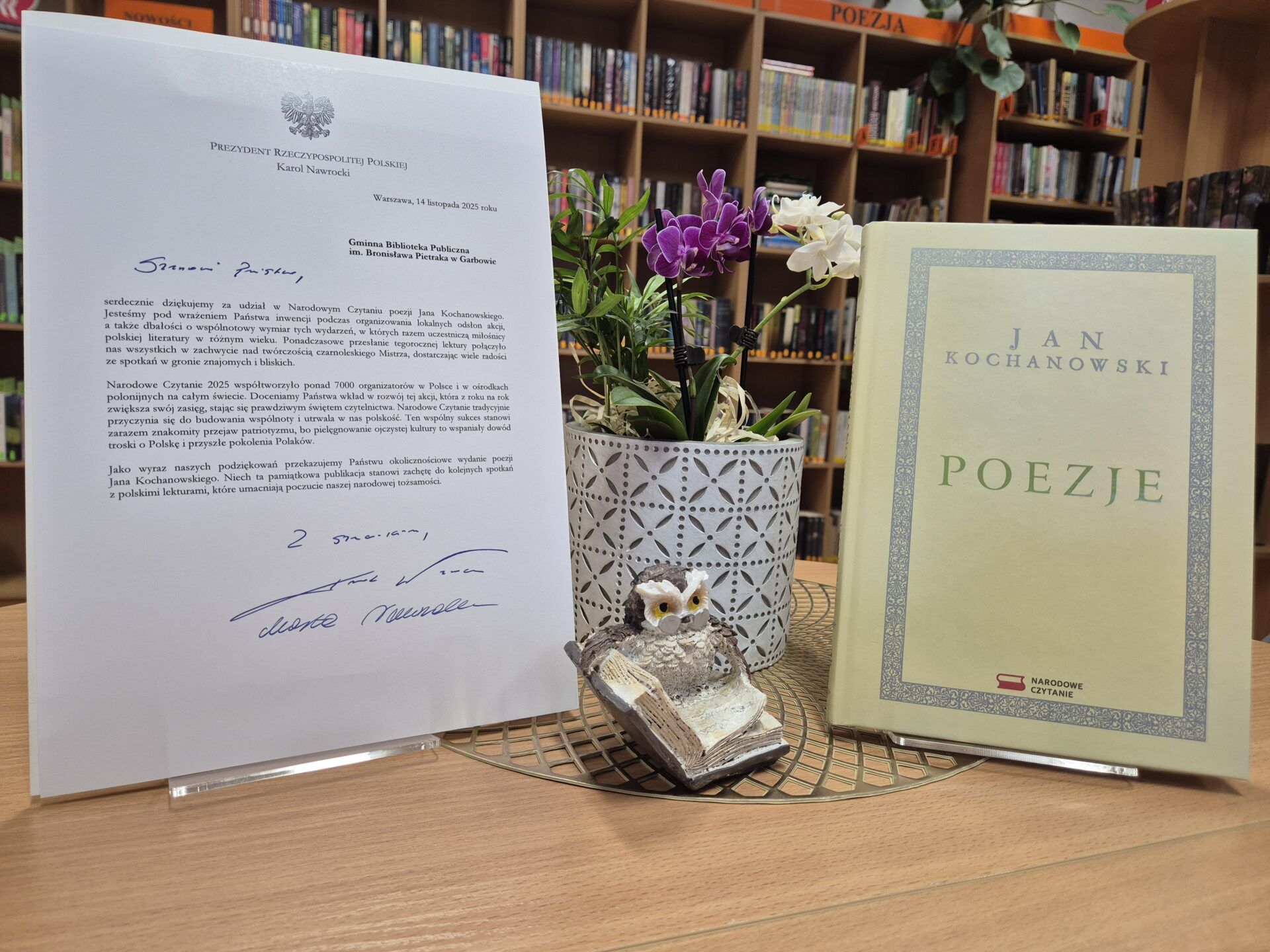 List od Pary Prezydenckiej, książka i kwiaty w doniczce na tle regałów bibliotecznych