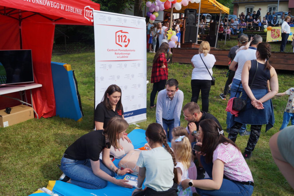 Stoisko numeru alarmowego: koordynatorki CPR w Lublinie przeprowadzające instruktaż udzielania pierwszej pomocy zainteresowanym dzieciom oraz rodzicom.