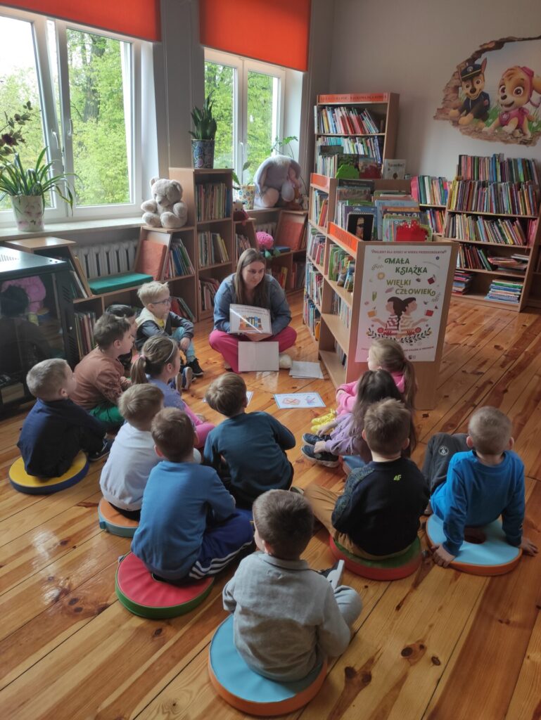 Grupa przedszkolaków siedzących na pączusiach podczas lekcji bibliotecznej z bibliotekarką.