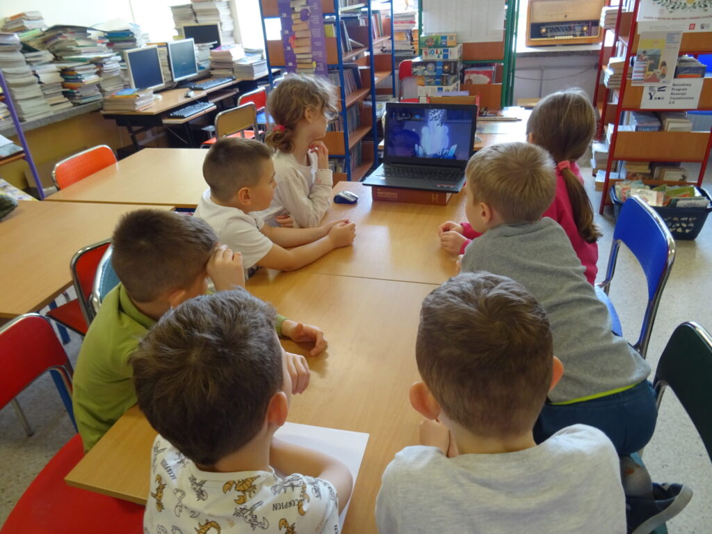 Siedmioro dzieci oglądających prezentacje na laptopie.