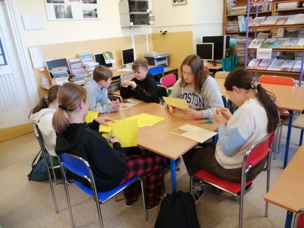 Sześcioro dzieci wykonujących żonkile z papieru w szkolnej bibliotece.