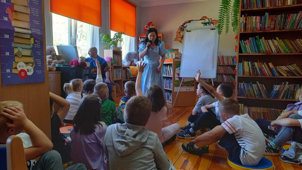 Grupa dzieci na spotkaniu autorskim z Edytą i Robertem Zarębskimi w wypożyczalni dla dzieci.