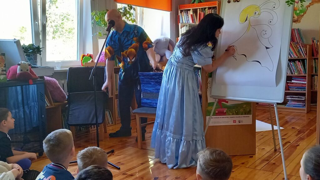 Grupa dzieci na spotkaniu autorskim z Edytą i Robertem Zarębskimi w wypożyczalni dla dzieci.