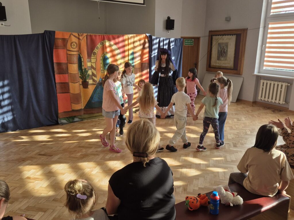 Grupa dzieci wraz z aktorami podczas przedstawienia teatralnego "Latający Kufer"