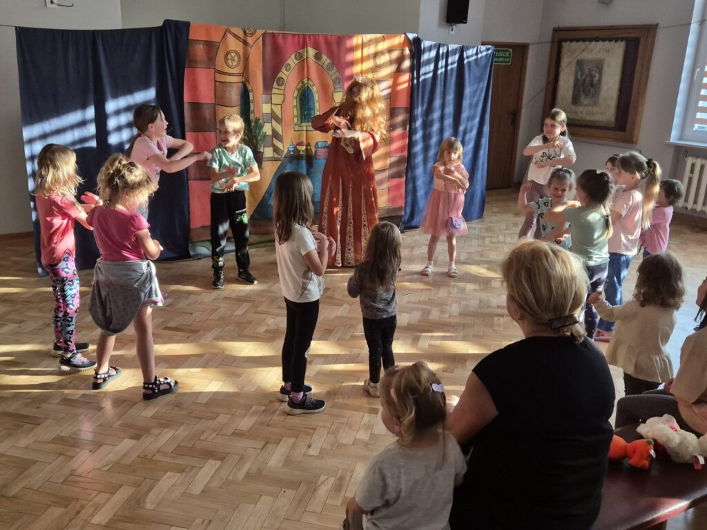 Grupa dzieci wraz z aktorami podczas przedstawienia teatralnego "Latający Kufer"