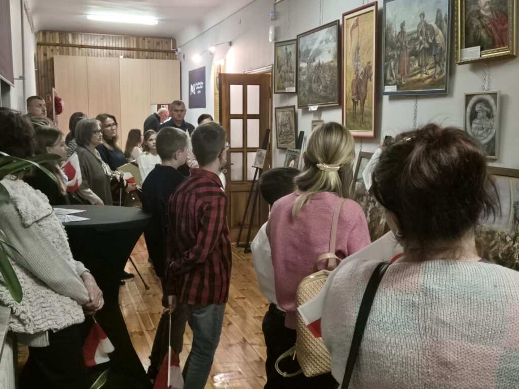Uczestnicy biorący udział w obchodach Święta Niepodległości w bibliotece, oglądający wystawę malarstwa K. Zlot.