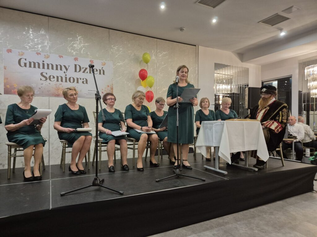 Seniorzy z Koła Rencistów i emerytów w zagrodach biorący udział w Narodowym Czytaniu podczas Gminnego Dnia Seniora