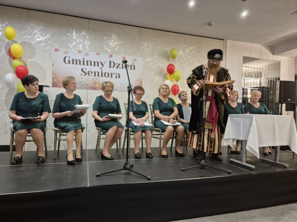 Seniorzy z Koła Rencistów i emerytów w zagrodach biorący udział w Narodowym Czytaniu podczas Gminnego Dnia Seniora