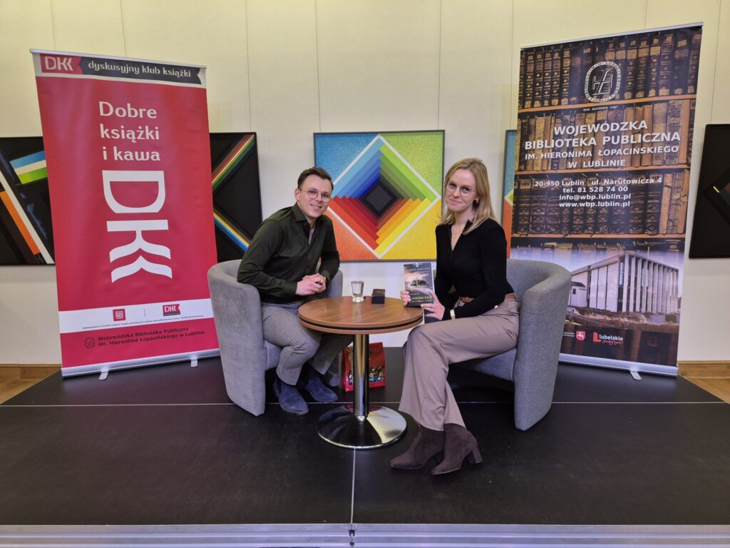 Mężczyzna i kobieta podczas spotkania autorskiego. W tle dwa banery DKK i WBP.