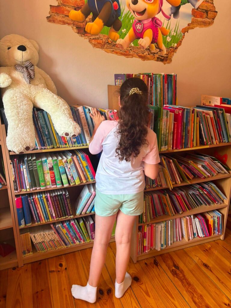 dziewczynka szukająca książki na regale bibliotecznych