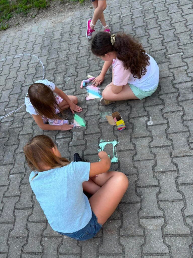 cztery dziewczynki rysujące kredą na kostce chodnikowej