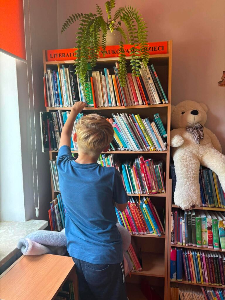 chłopiec przeglądający książki ustawione na regale bibliotecznym