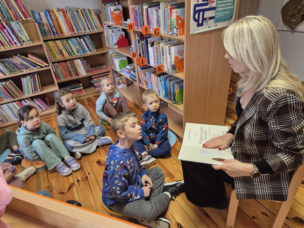 czwórka dzieci siedzących na pączusiach między regałami w bibliotece